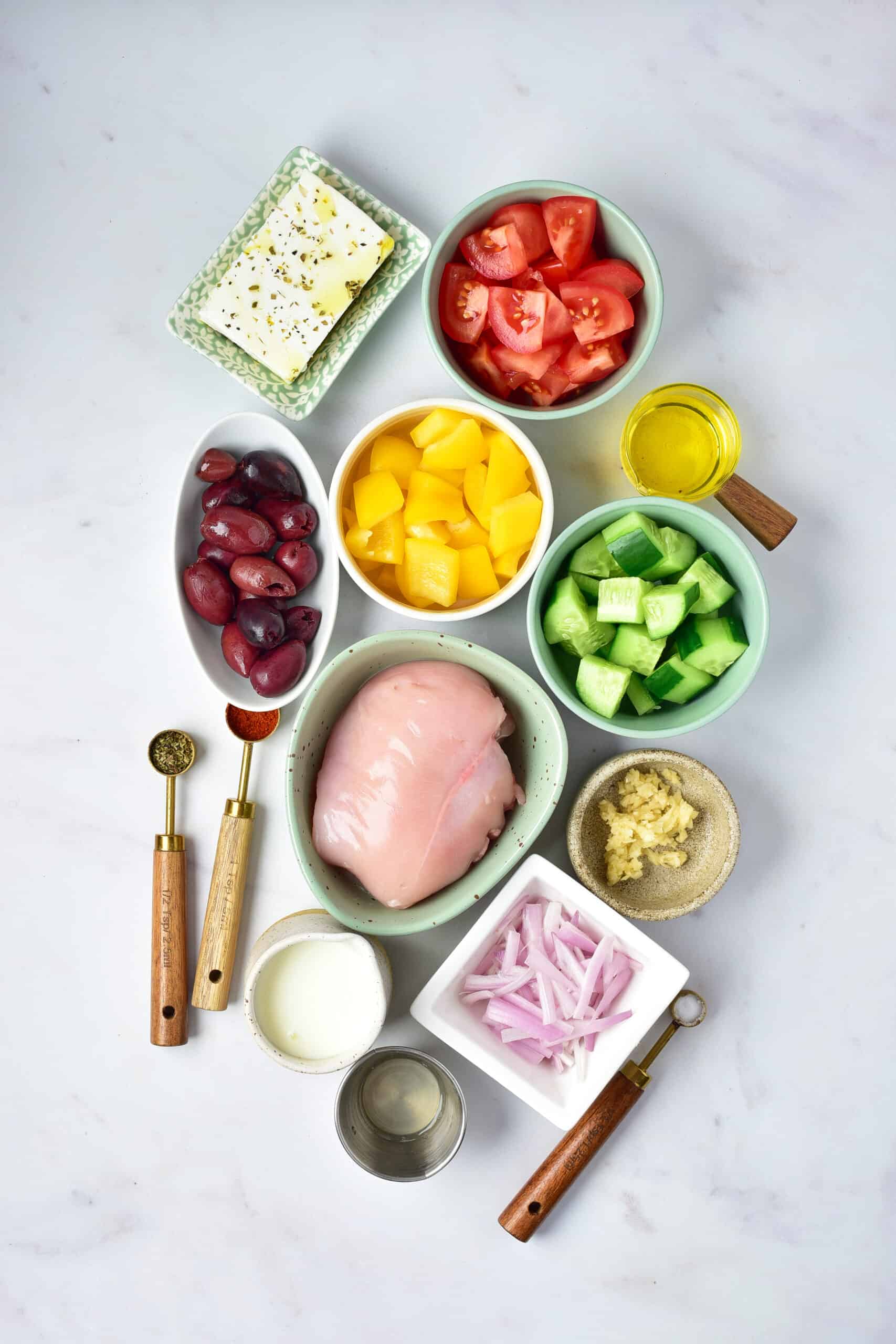 Greek Chicken Bowls featuring chicken breast, diced tomatoes, cucumbers, yellow bell peppers, kalamata olives, feta cheese, and more are served on a white surface—perfect for your next air fryer creation.