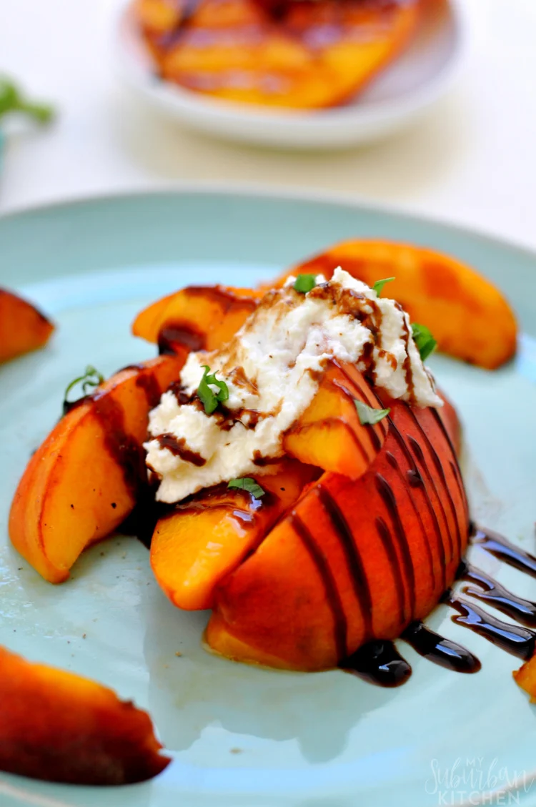 Sliced peaches topped with whipped ricotta, fresh herbs, and a drizzle of balsamic glaze make for an elegant peach dessert on a light blue plate.