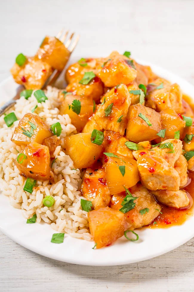 A plate of brown rice served with sweet and sour chicken, pineapple chunks, chopped green onions, and cilantro garnish—an ideal slow cooker dish for easy summer recipes.