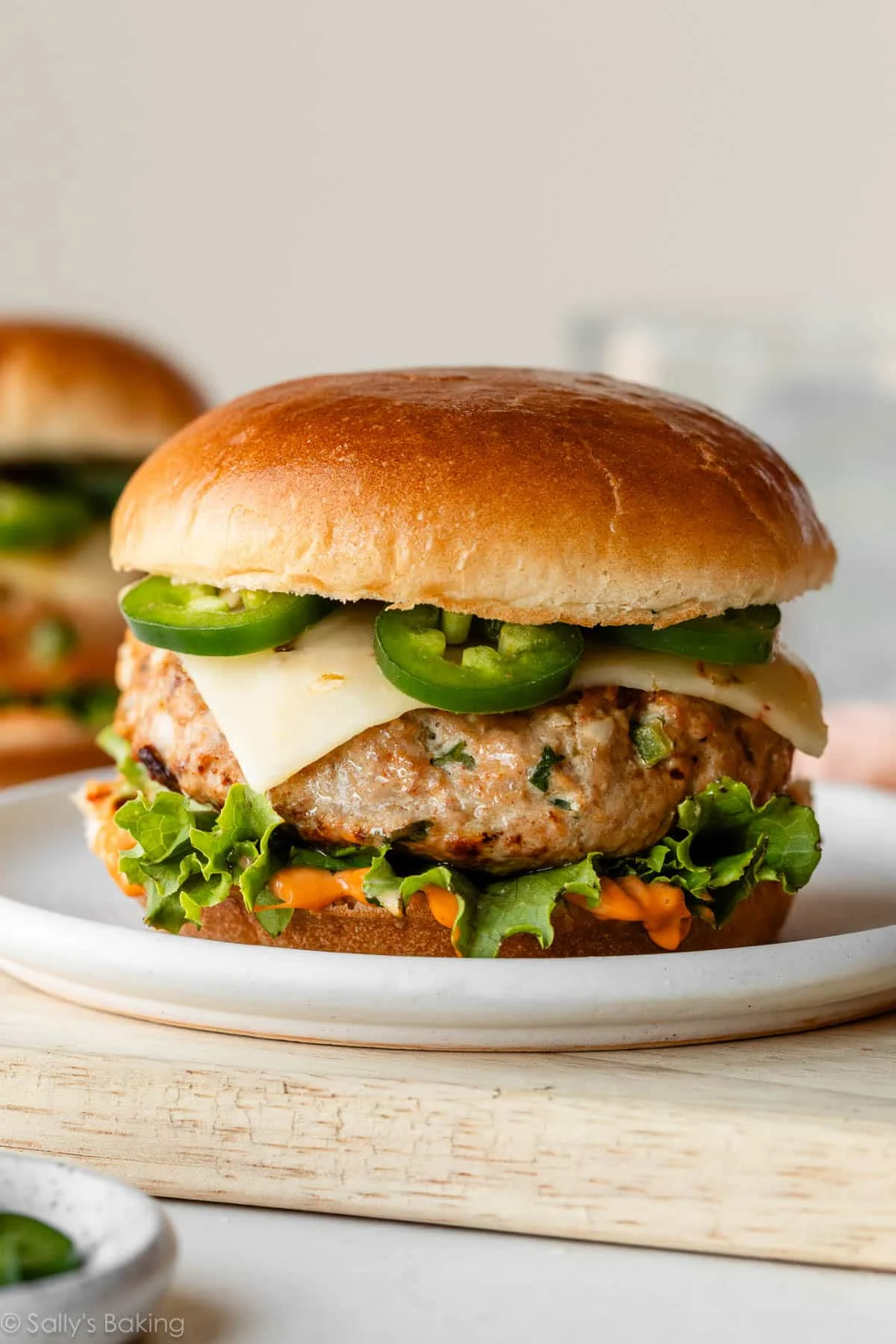 A healthy chicken burger with lettuce, cheese, sliced jalapeños, and sauce on a brioche bun, served on a white plate—perfect for light dinners.