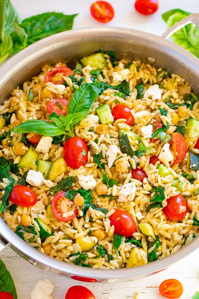 A stainless steel pot filled with orzo pasta salad—cherry tomatoes, chickpeas, feta cheese, spinach, cucumber, and fresh basil—perfect for cooler meals or as refreshing boat food on your next boat day.