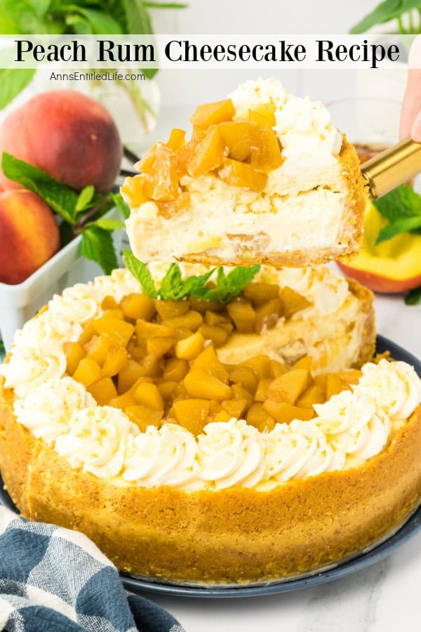 A slice of peach rum cheesecake, a delectable peach dessert topped with peach chunks, is being lifted from a whole cheesecake, surrounded by fresh peaches and a blue cloth.