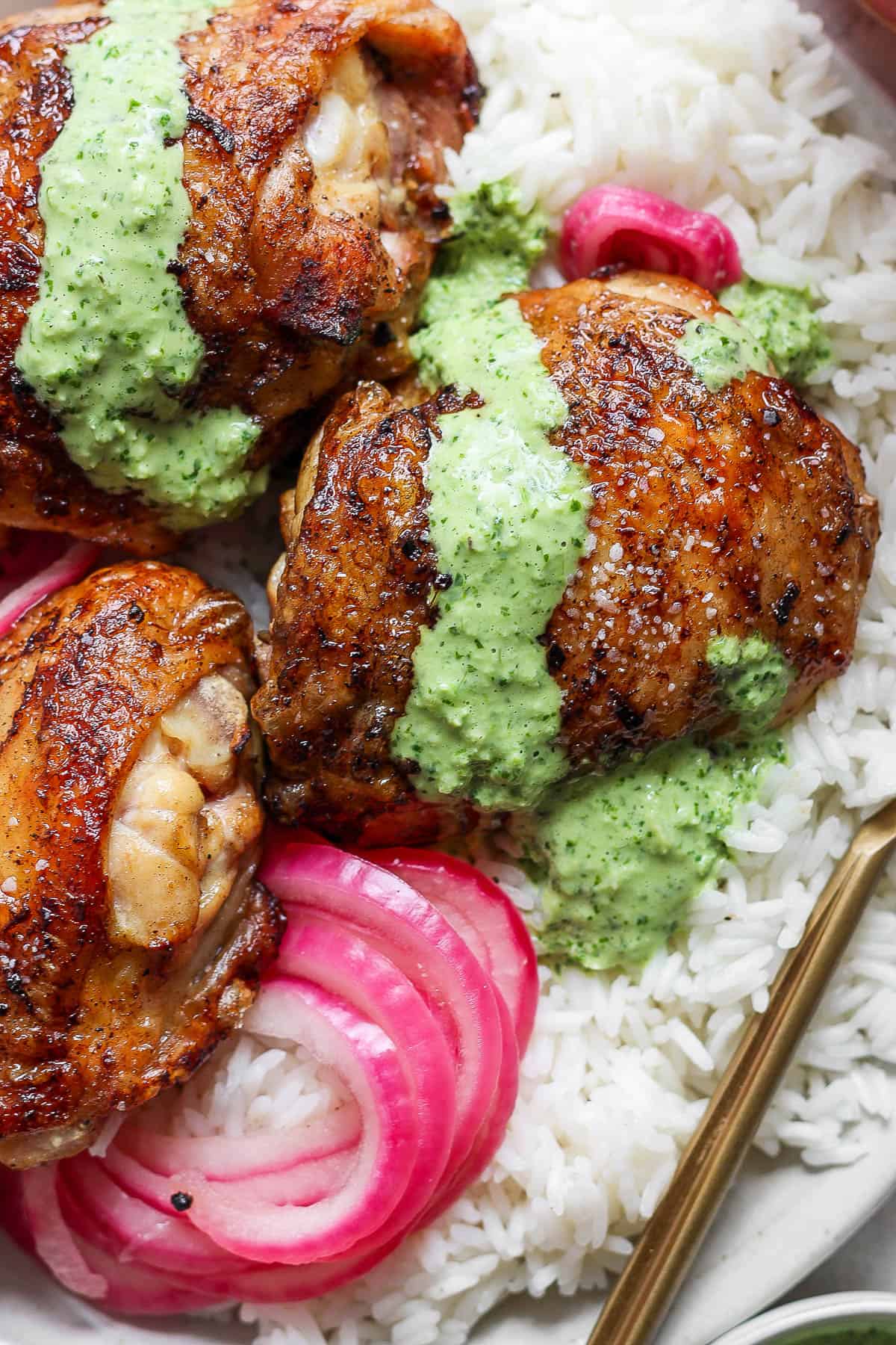 Three pieces of seasoned, grilled chicken with green sauce served over white rice and pickled red onions—a perfect summer dish.