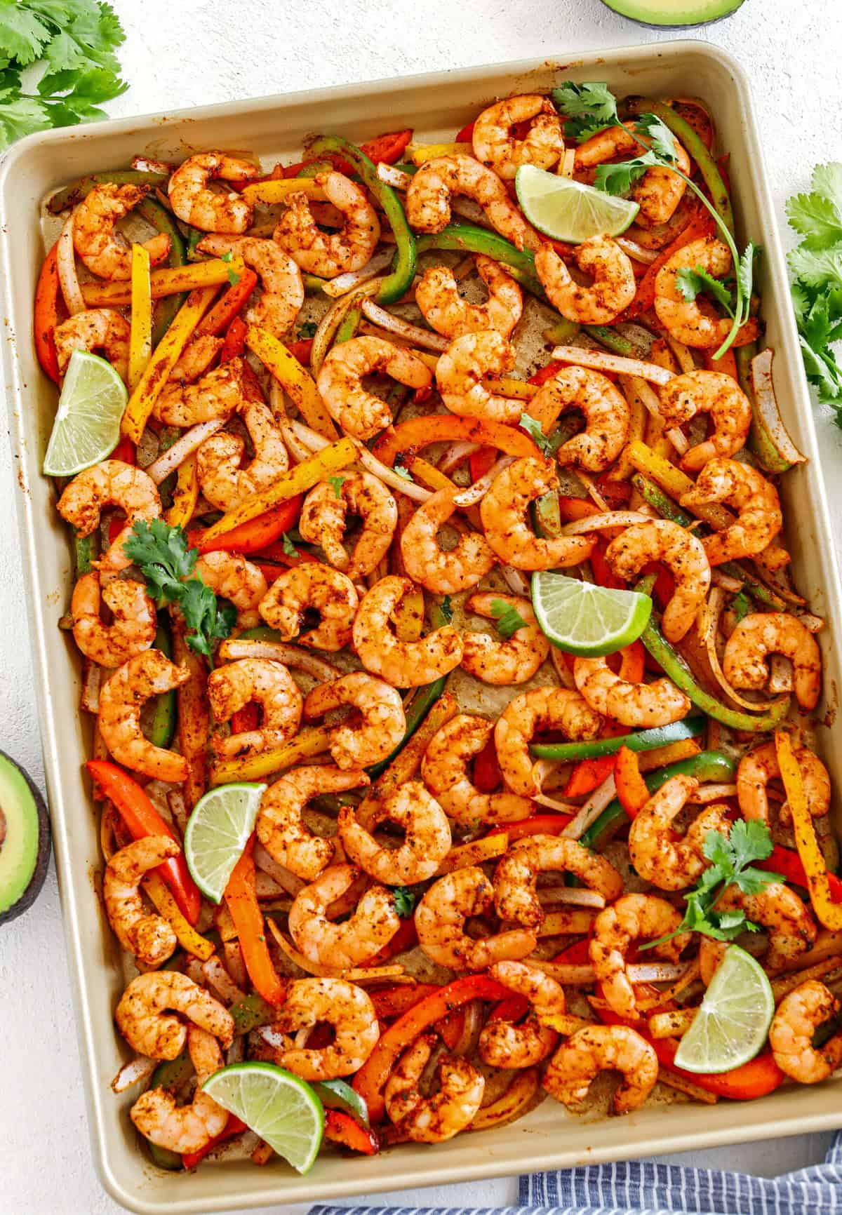 Baked shrimp fajitas with sliced bell peppers and onions on a sheet pan, garnished with lime wedges and cilantro—perfect for an easy summer dinner.