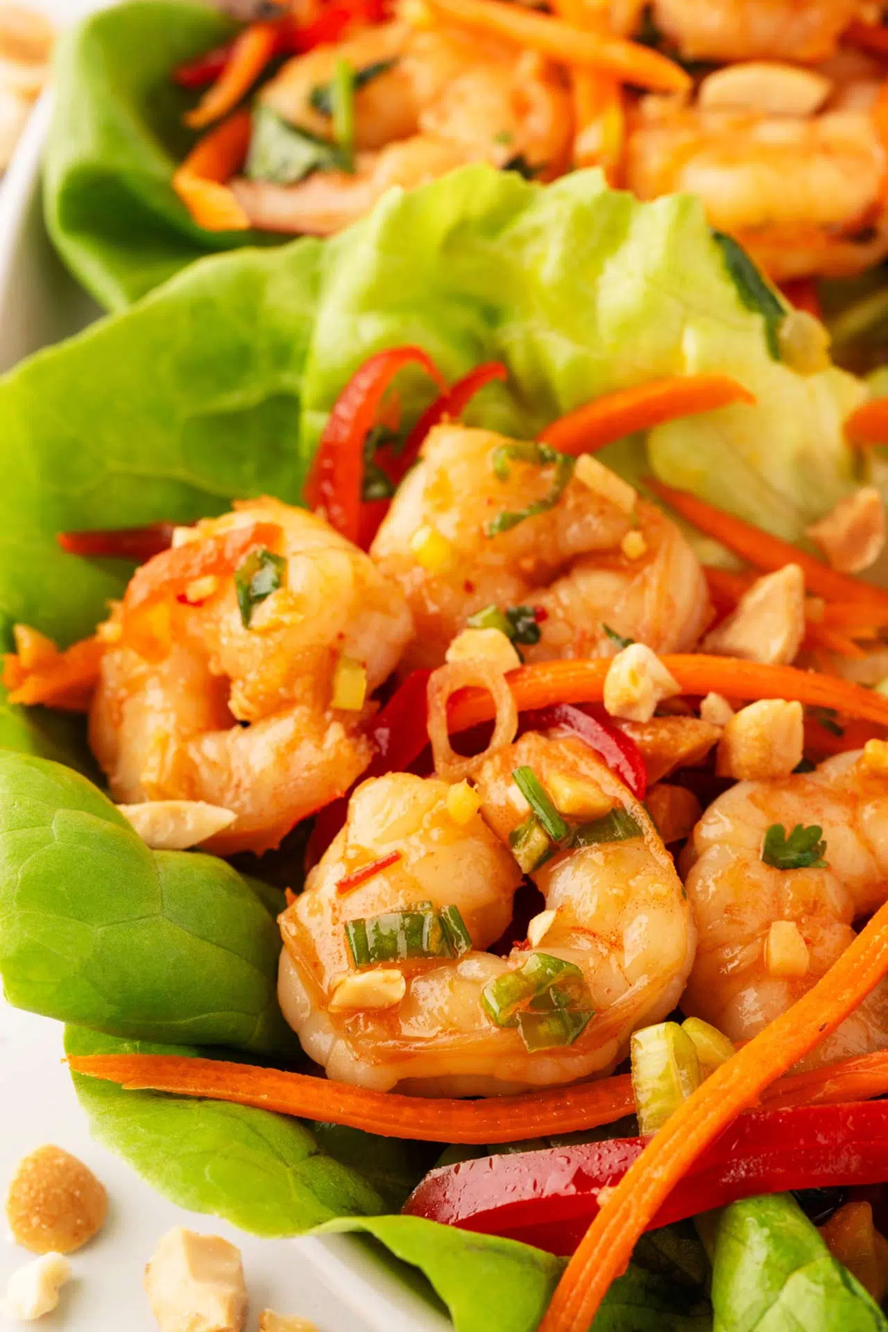 Enjoy a refreshing summer dinner with shrimp lettuce wraps, featuring sliced carrots, red peppers, green onions, and chopped peanuts on a crisp lettuce leaf.