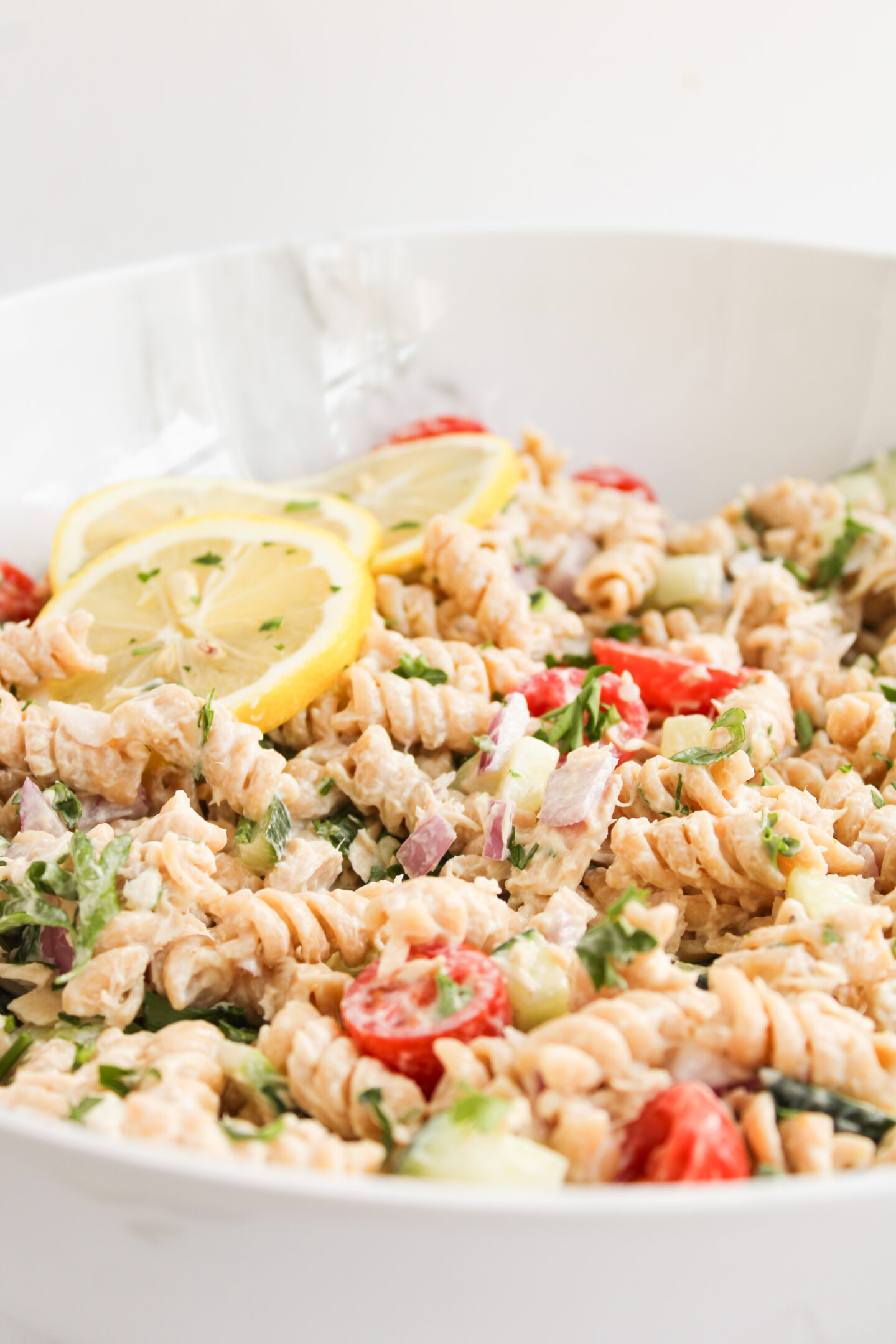 A bowl of rotini pasta salad with chopped vegetables, herbs, cherry tomatoes, and lemon slices as garnish—perfect for beach picnic food or tasty beach lunch ideas.