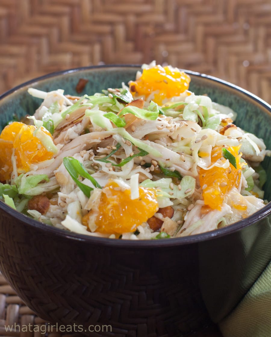 A bowl of chicken salad with shredded chicken, cabbage, orange segments, green onions, and sesame seeds—perfect for summer recipes and refreshing cold chicken recipes.