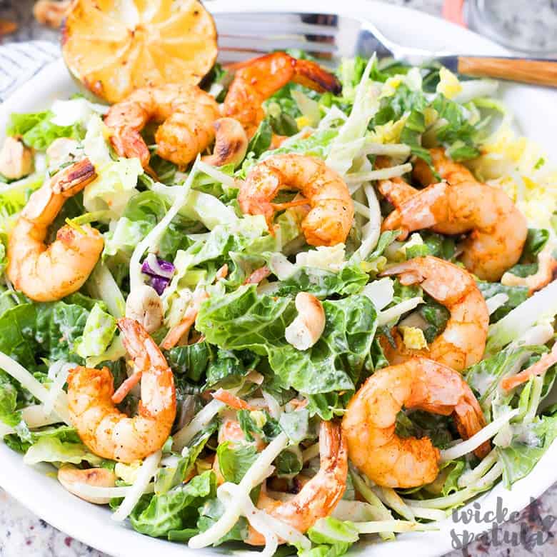 A perfect summer dinner: a salad with grilled shrimp, leafy greens, shredded vegetables, crunchy cashews, and a grilled lemon half on top.