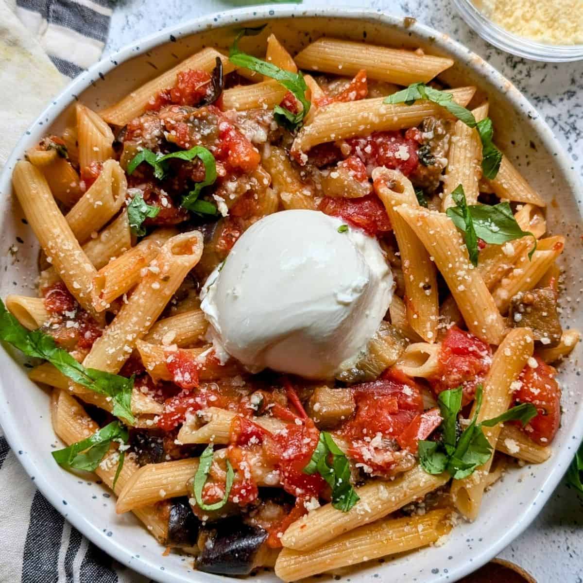 A bowl of penne pasta with tomato sauce, grilled vegetables, fresh basil, grated cheese, and a ball of burrata in the center—perfect for Italian Summer Recipes.