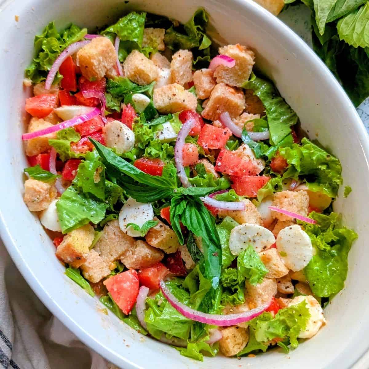 A bowl of salad with lettuce, tomato, red onion, mozzarella balls, croutons, and fresh basil, seasoned with black pepper—perfect for Italian Summer Recipes.