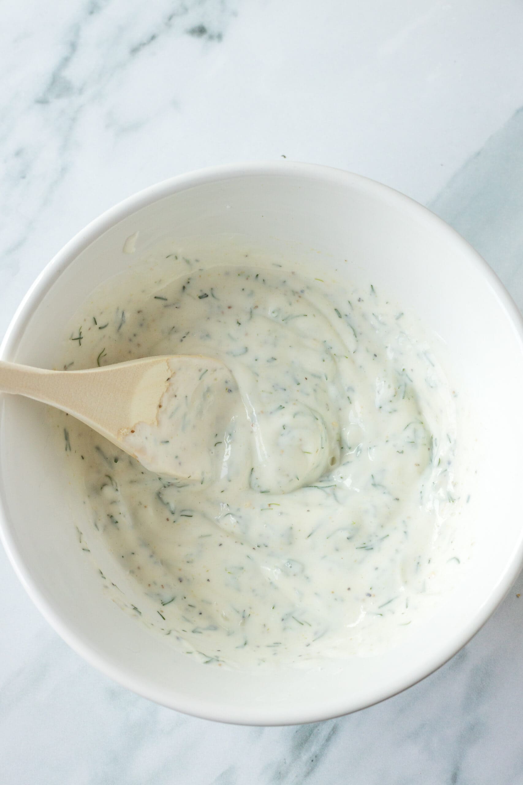Creamy ranch dressing mixed with fresh dill in a bowl.