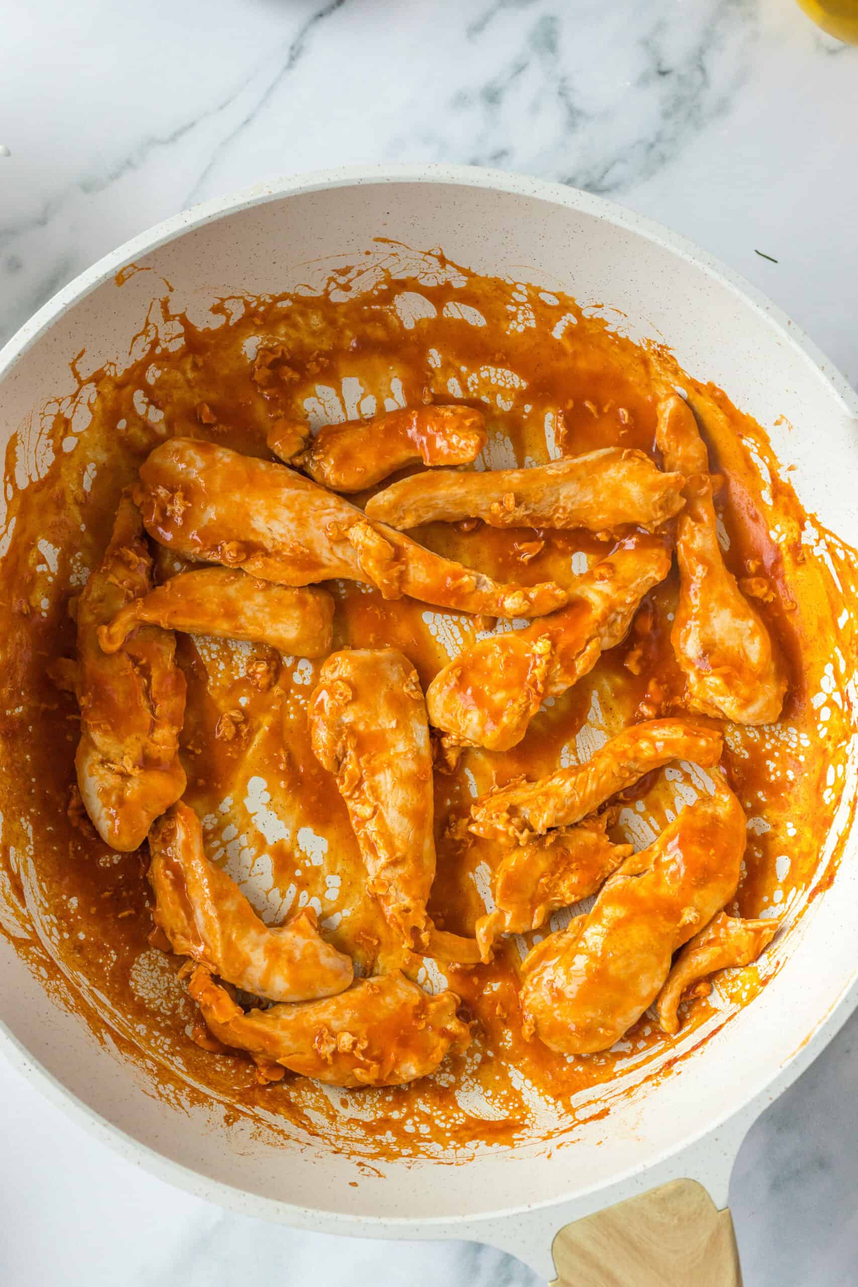 Cooked chicken tossed in buffalo sauce in a skillet.