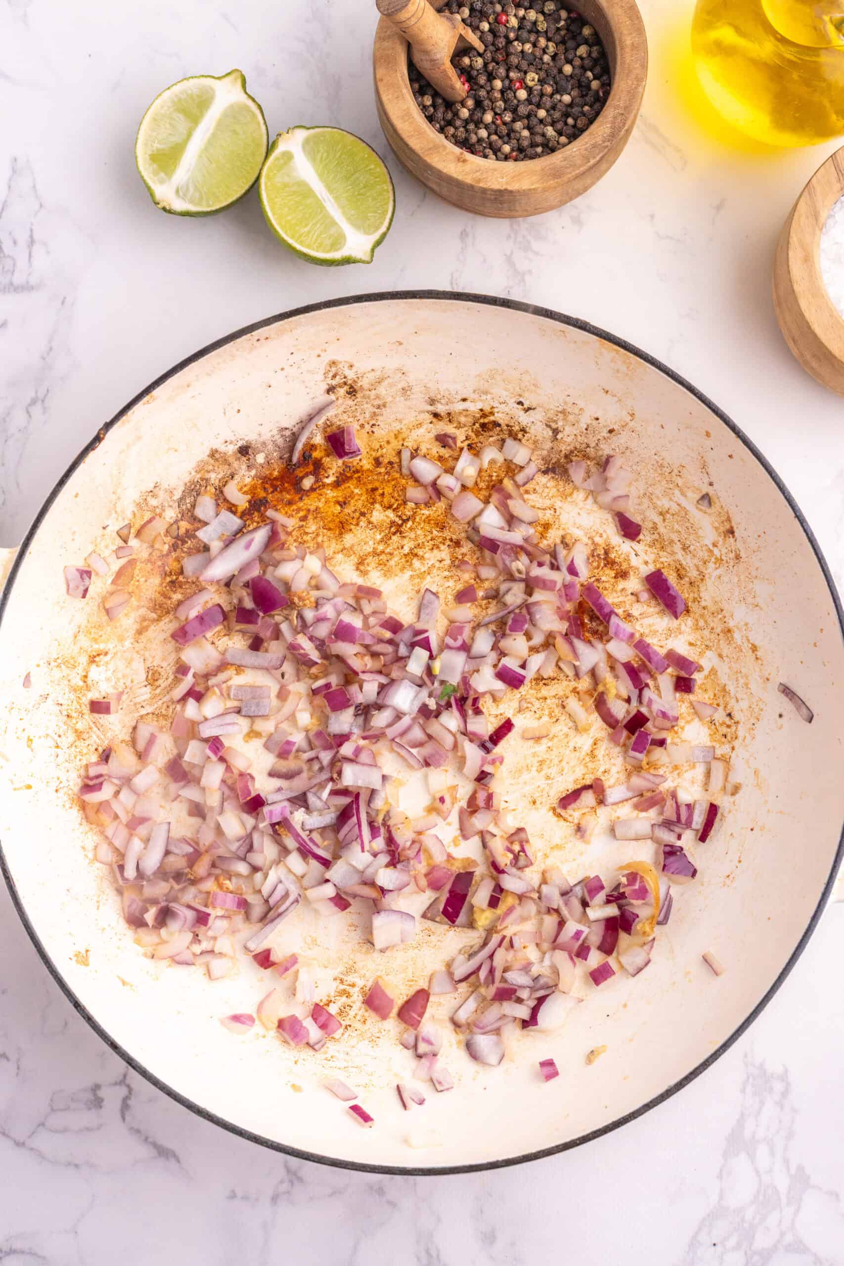 Chopped red onion sautéing in a skillet with garlic and ginger.