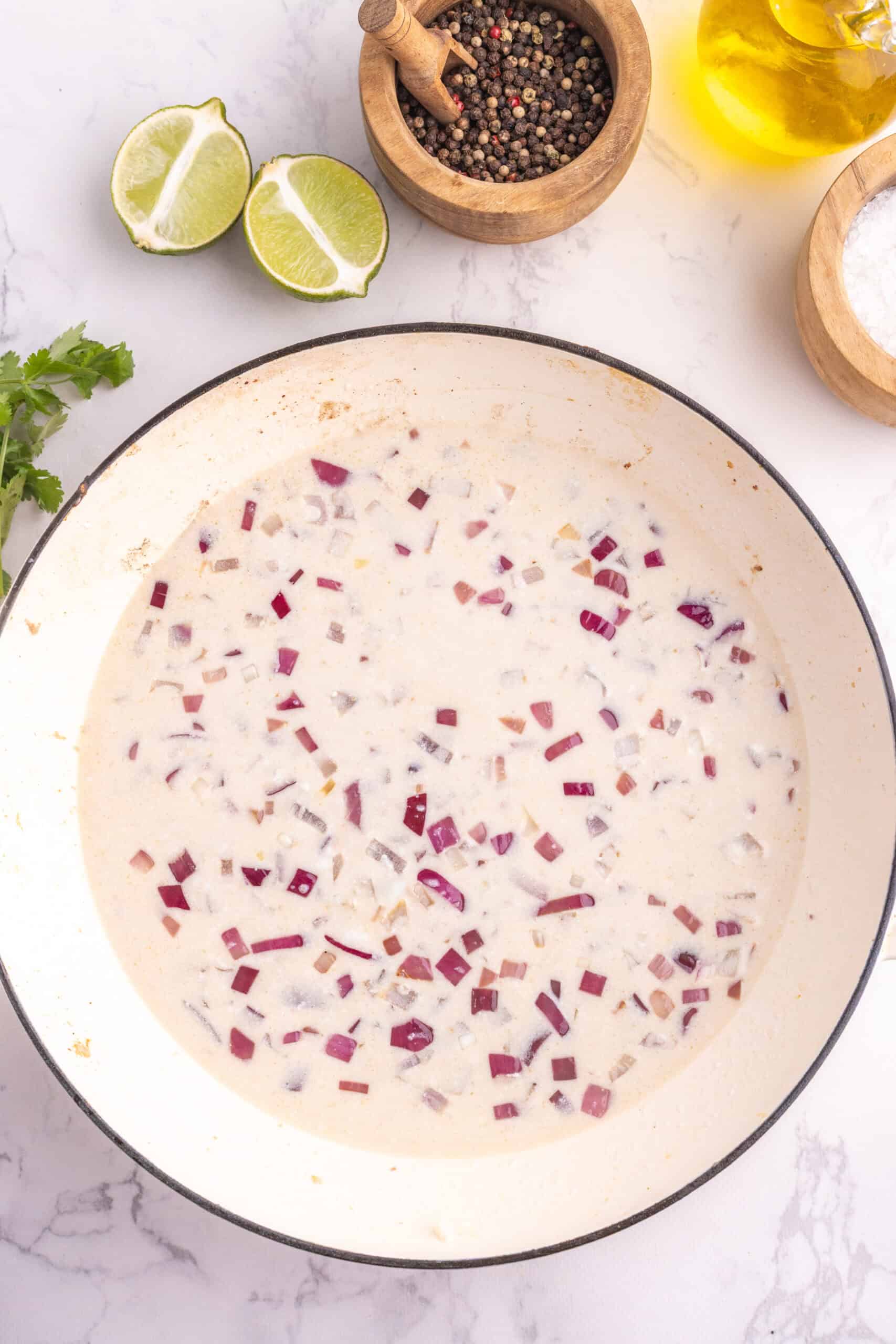 Coconut milk sauce simmering with red onion in a skillet.