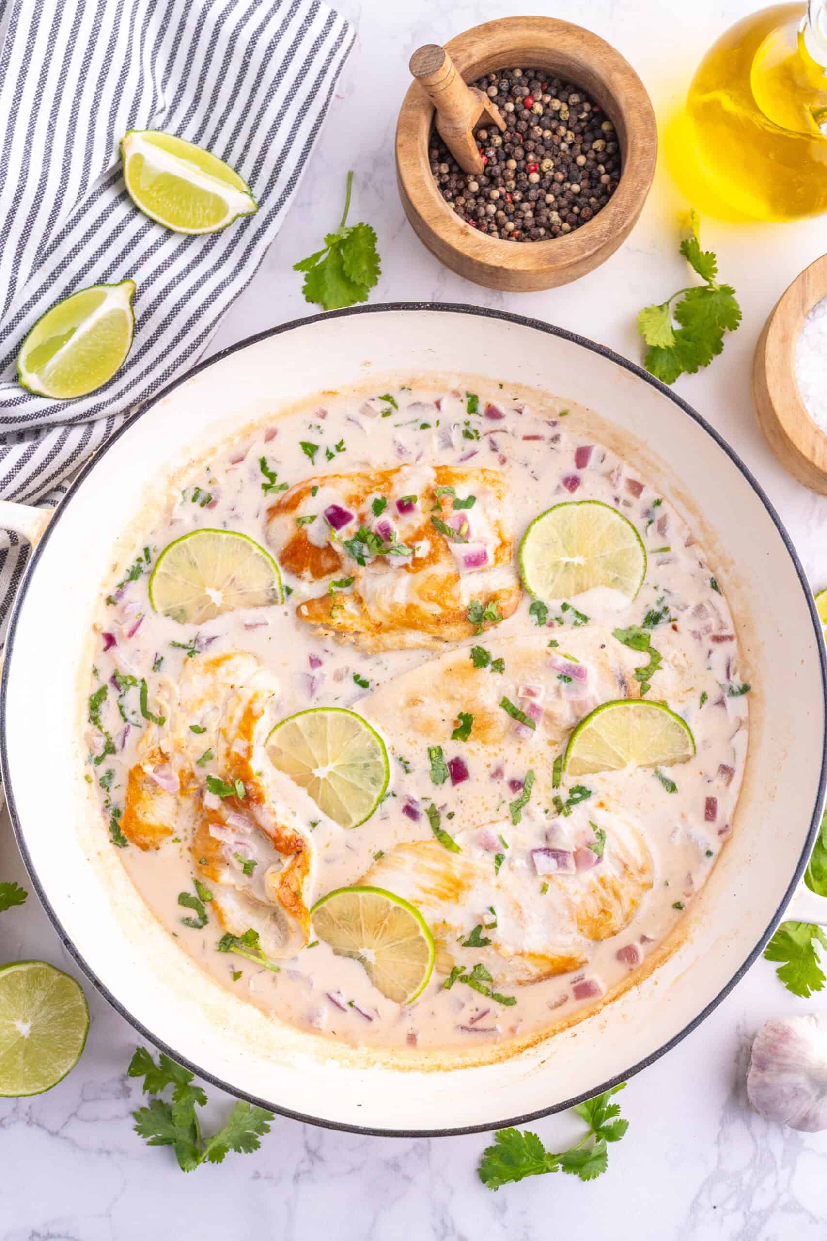 Chicken simmering in creamy coconut lime sauce with lime slices and cilantro.