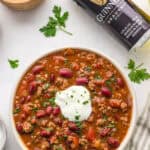 Guinness chili served in a bowl with sour cream, parsley, kidney beans, tomatoes, and ground beef.