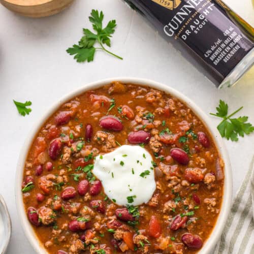 Guinness chili served in a bowl with sour cream, parsley, kidney beans, tomatoes, and ground beef.