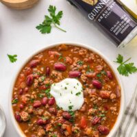 Guinness chili served in a bowl with sour cream, parsley, kidney beans, tomatoes, and ground beef.