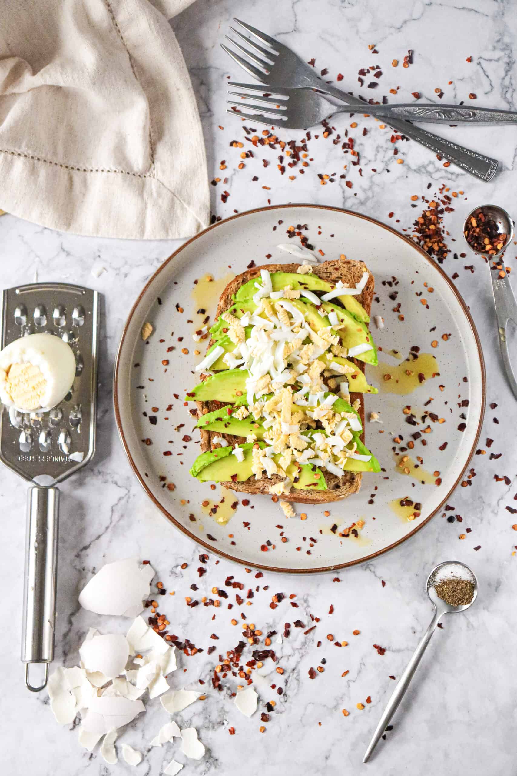 Hard-boiled egg being grated beside avocado toast.
