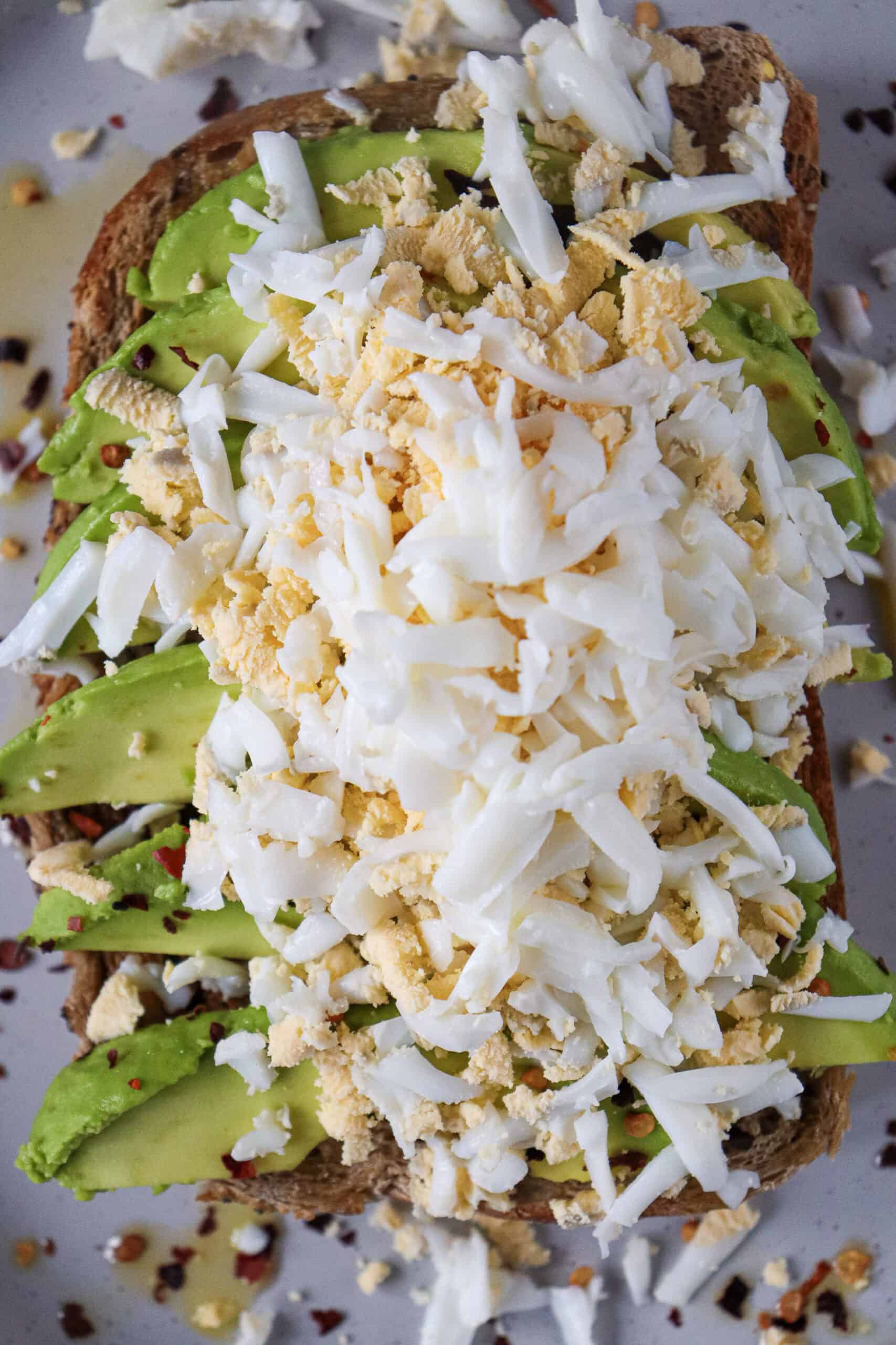 Freshly grated hard-boiled egg piled over sliced avocado toast.