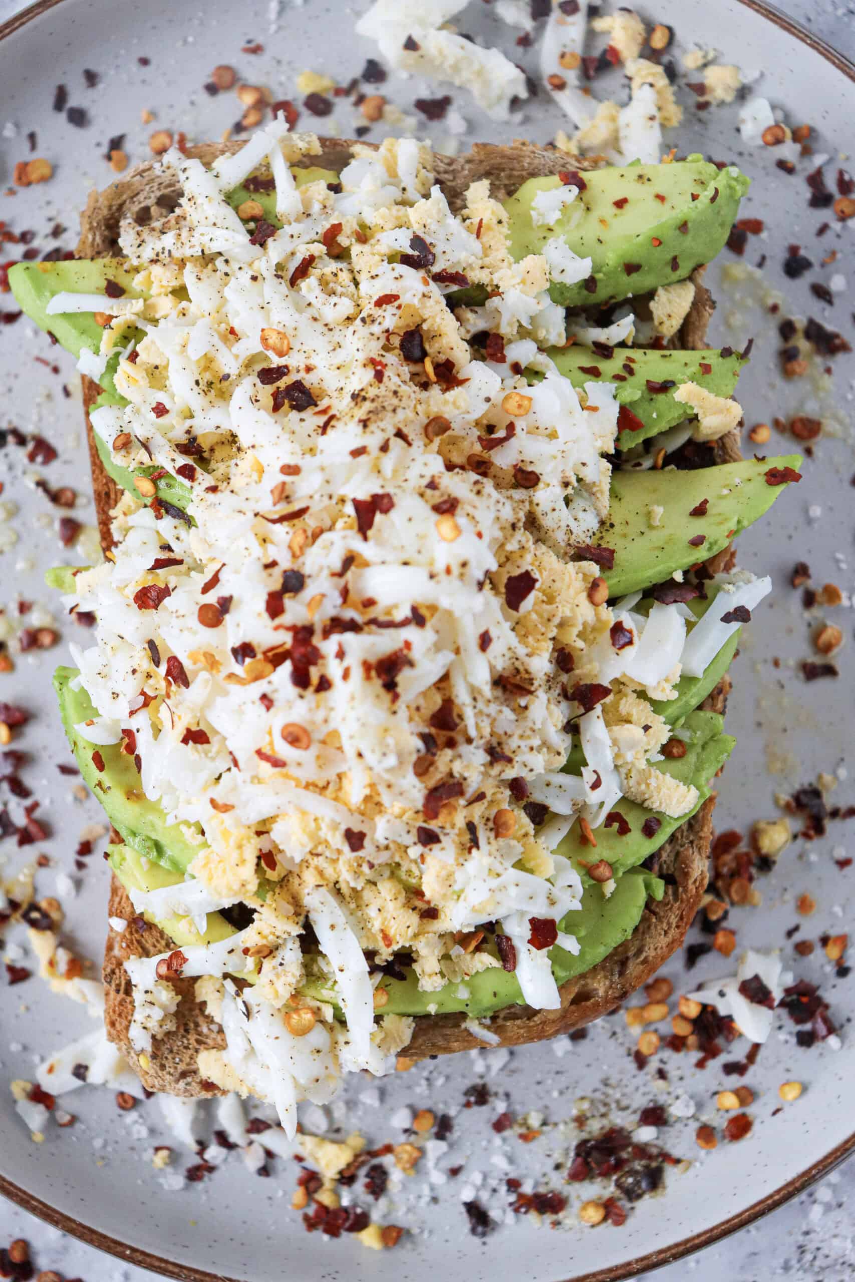 Grated egg avocado toast seasoned with chili flakes, salt, and pepper.