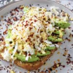 Grated hard-boiled egg and sliced avocado on toast with chili flakes.