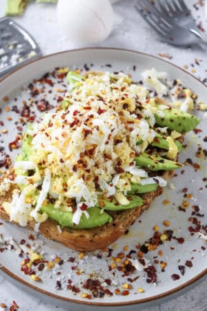 Grated hard-boiled egg and sliced avocado on toast with chili flakes.