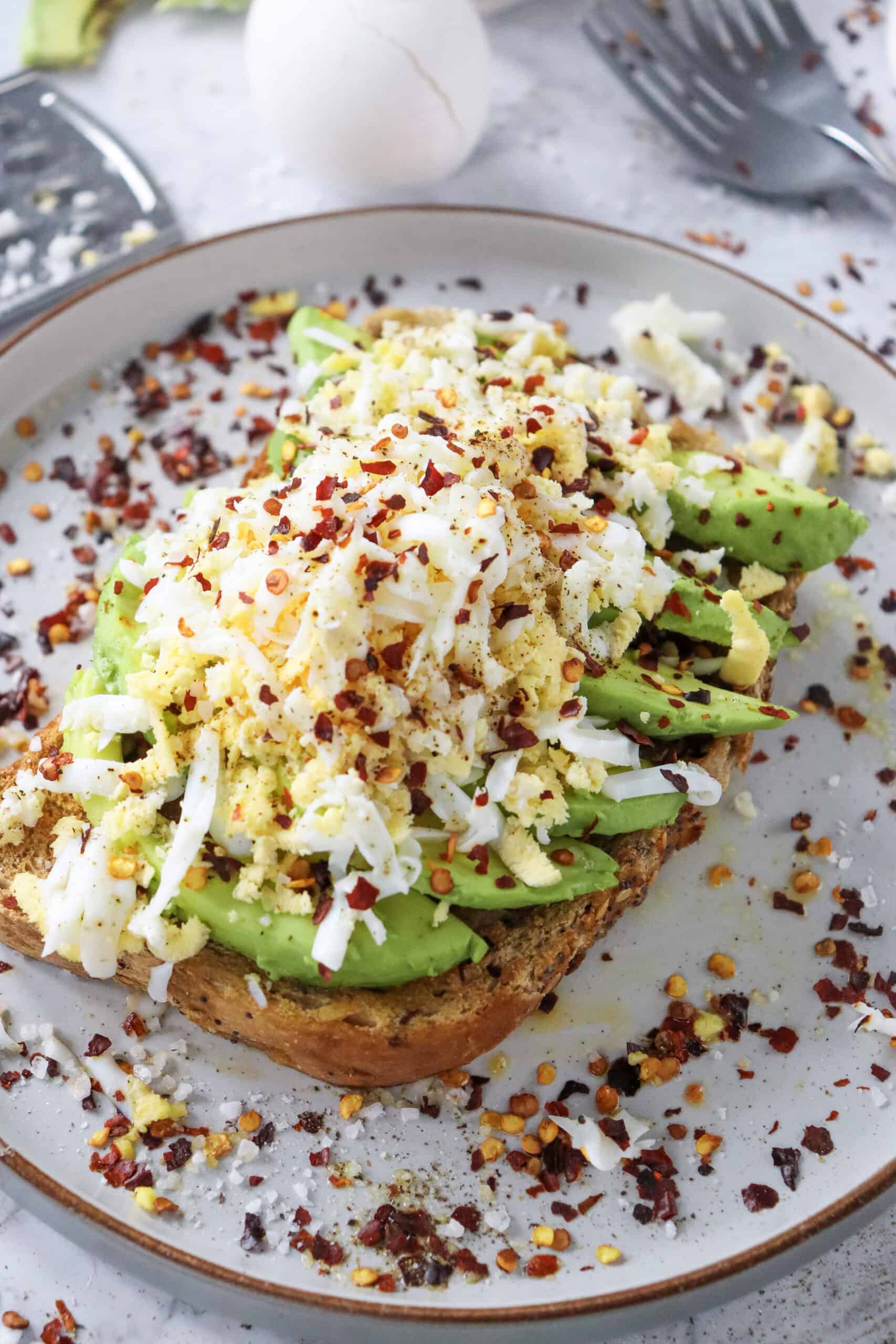 Grated hard-boiled egg and sliced avocado on toast with chili flakes.