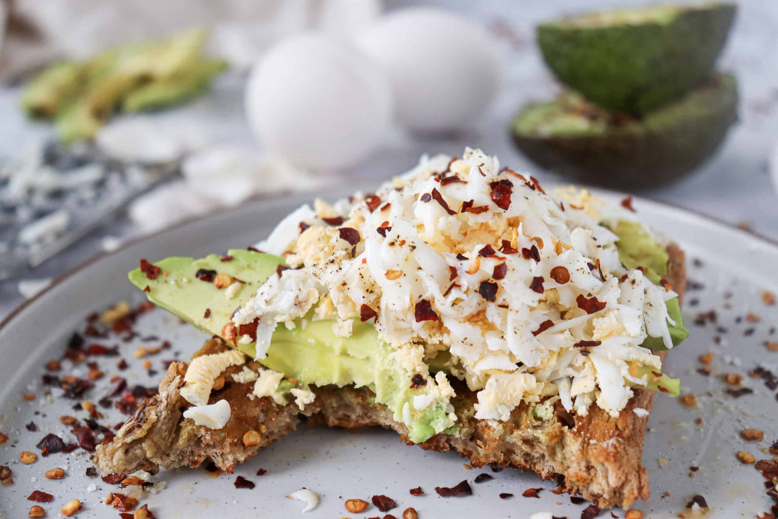A bitten slice of grated egg avocado toast with chili flakes.