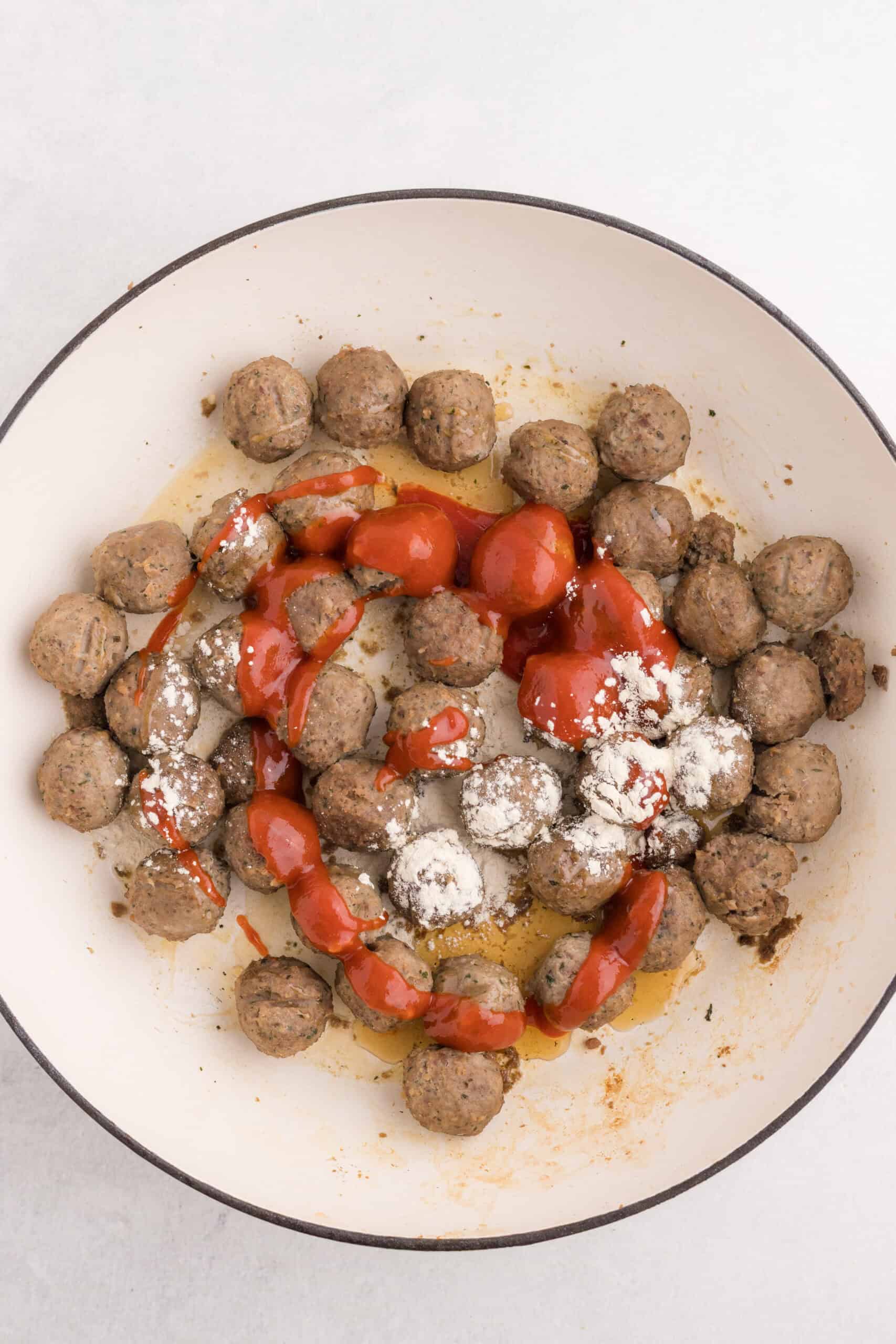 Sriracha, maple syrup, and garlic powder added to meatballs in a skillet.
