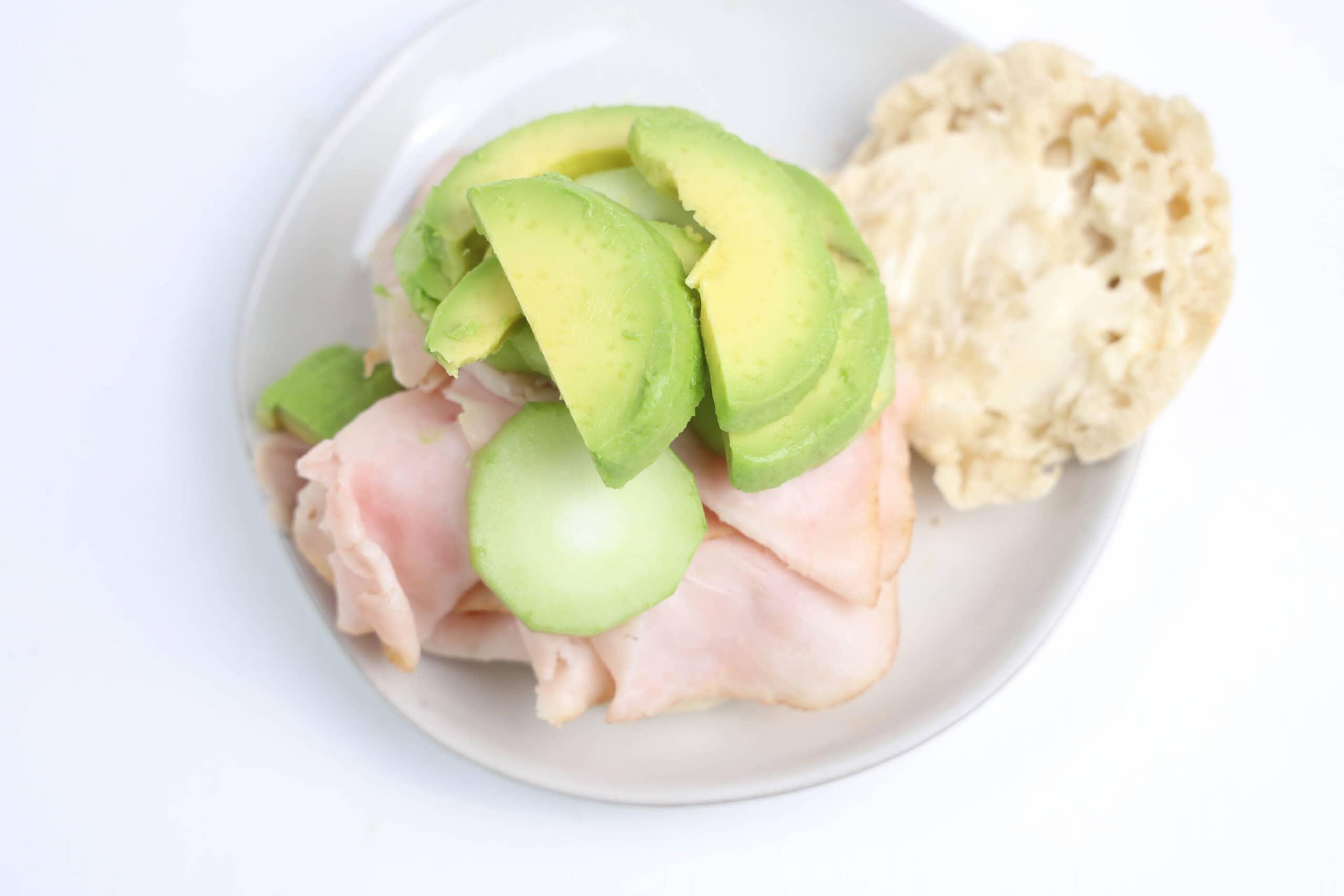 Avocado and cucumber layered over turkey on an English muffin.