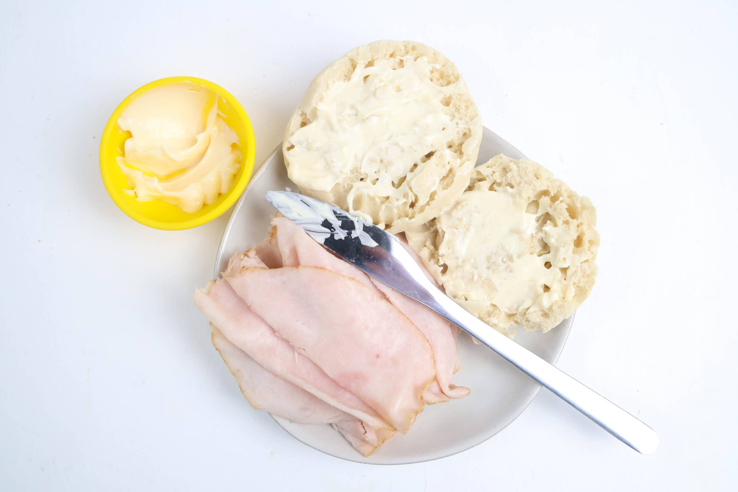 Mayonnaise spread on both halves of an English muffin.
