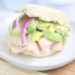 Turkey breakfast sandwich with avocado, cucumber, and red onion on an English muffin.