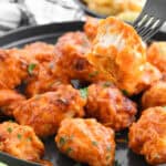 A fork holding a cut buffalo boneless wing over sauced chicken with celery and fries.