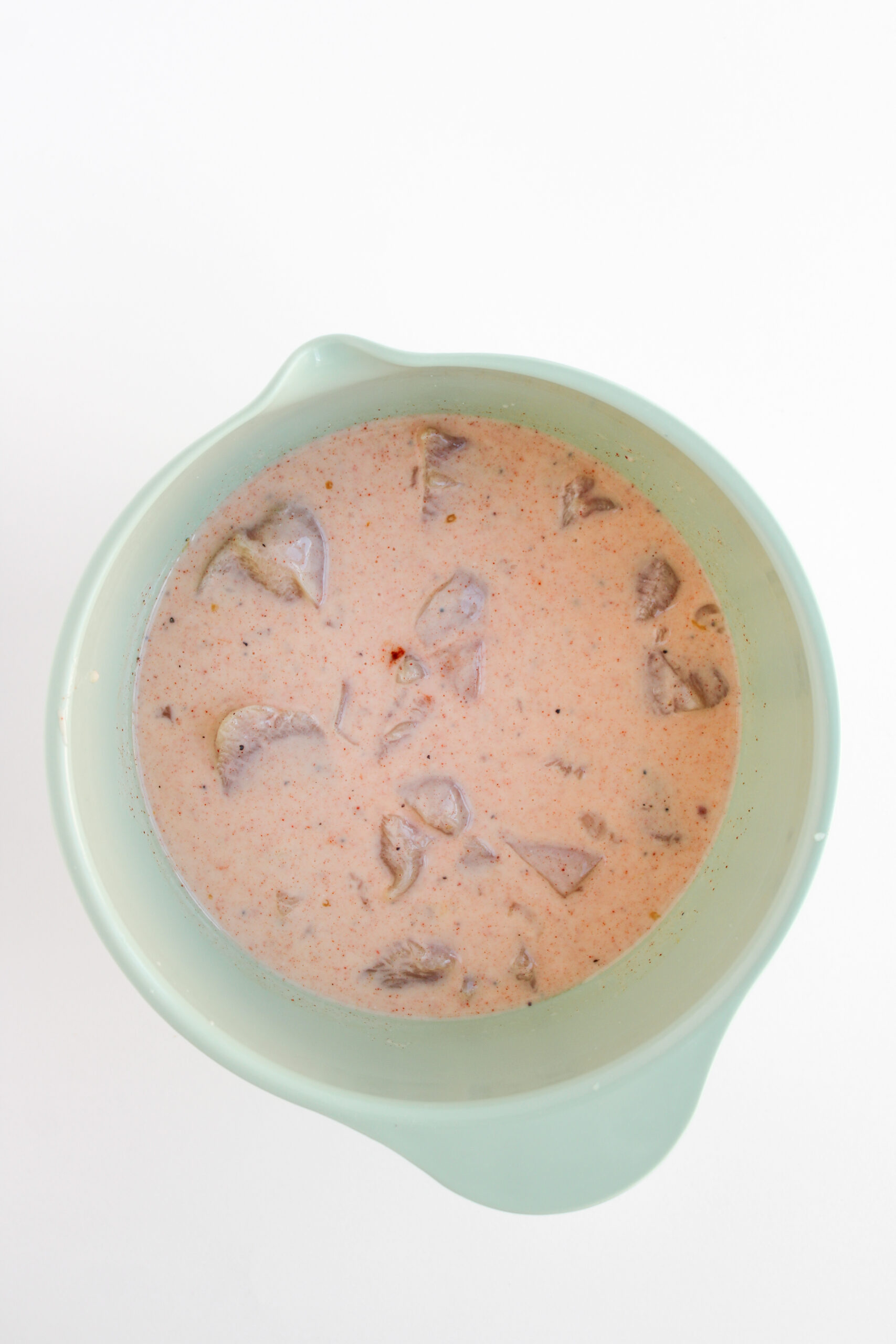 Chicken pieces marinating in a seasoned buttermilk mixture.