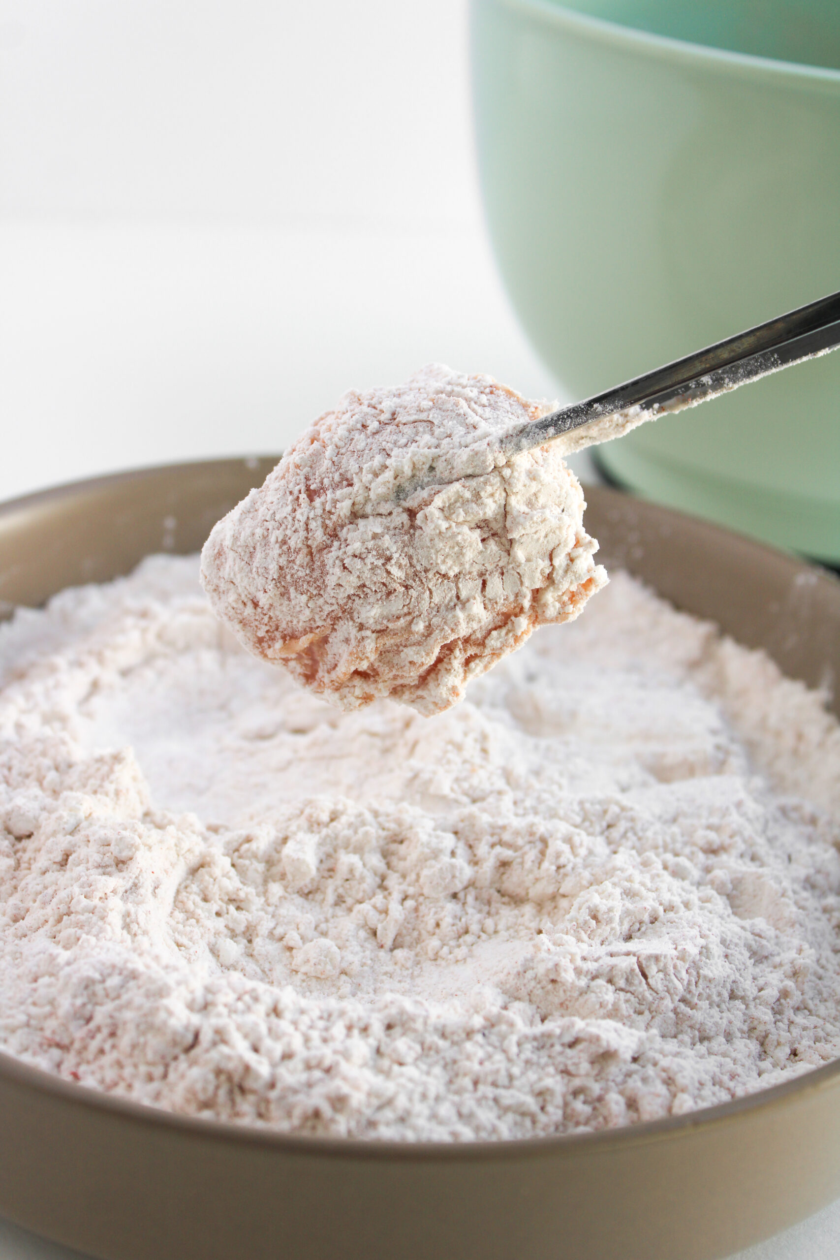 A piece of marinated chicken being coated in seasoned flour.