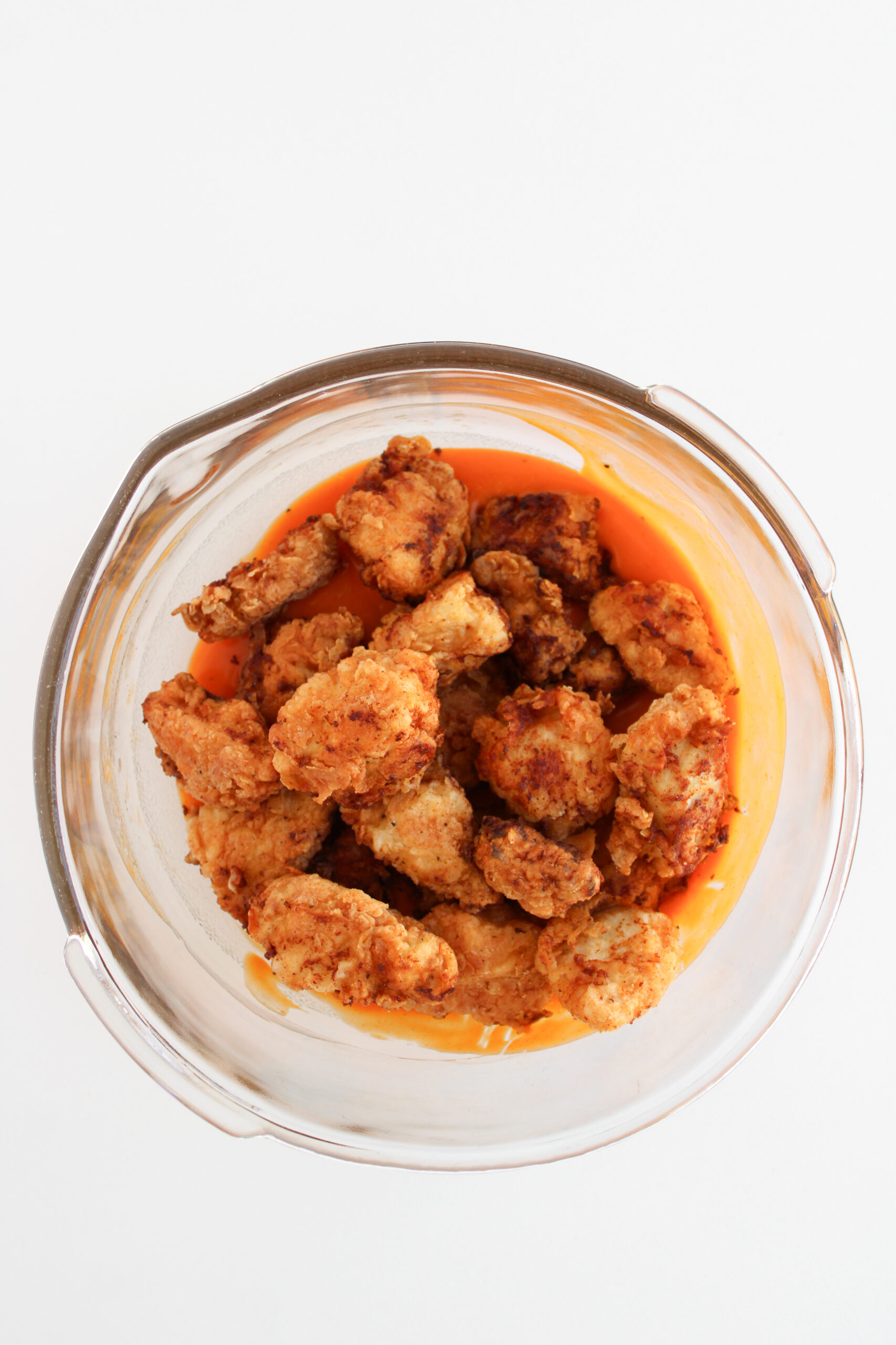 Fried boneless chicken pieces being tossed in buffalo sauce.