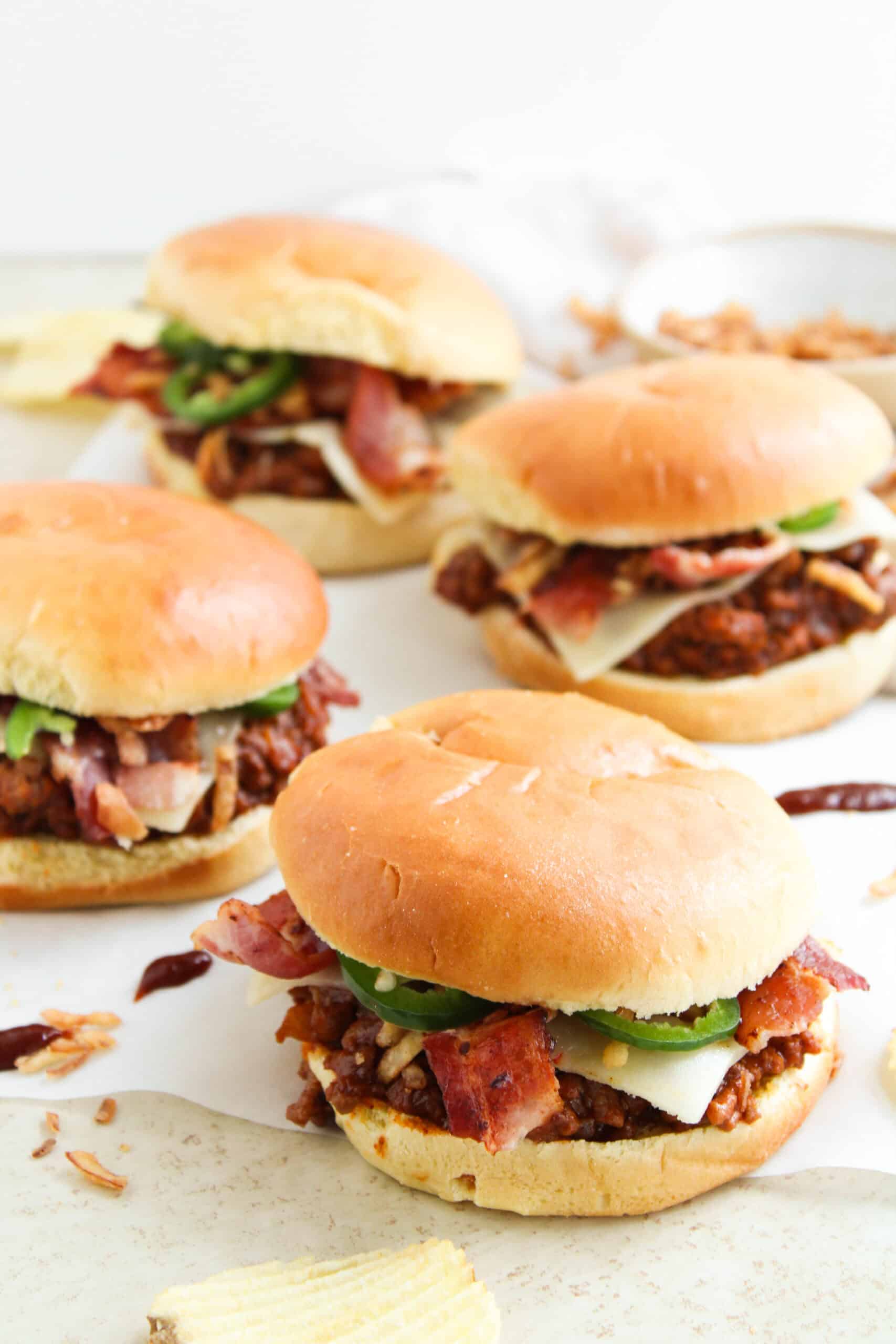Four BBQ cowboy sloppy joe sandwiches topped with cheese, bacon, jalapeños, and crispy onions.