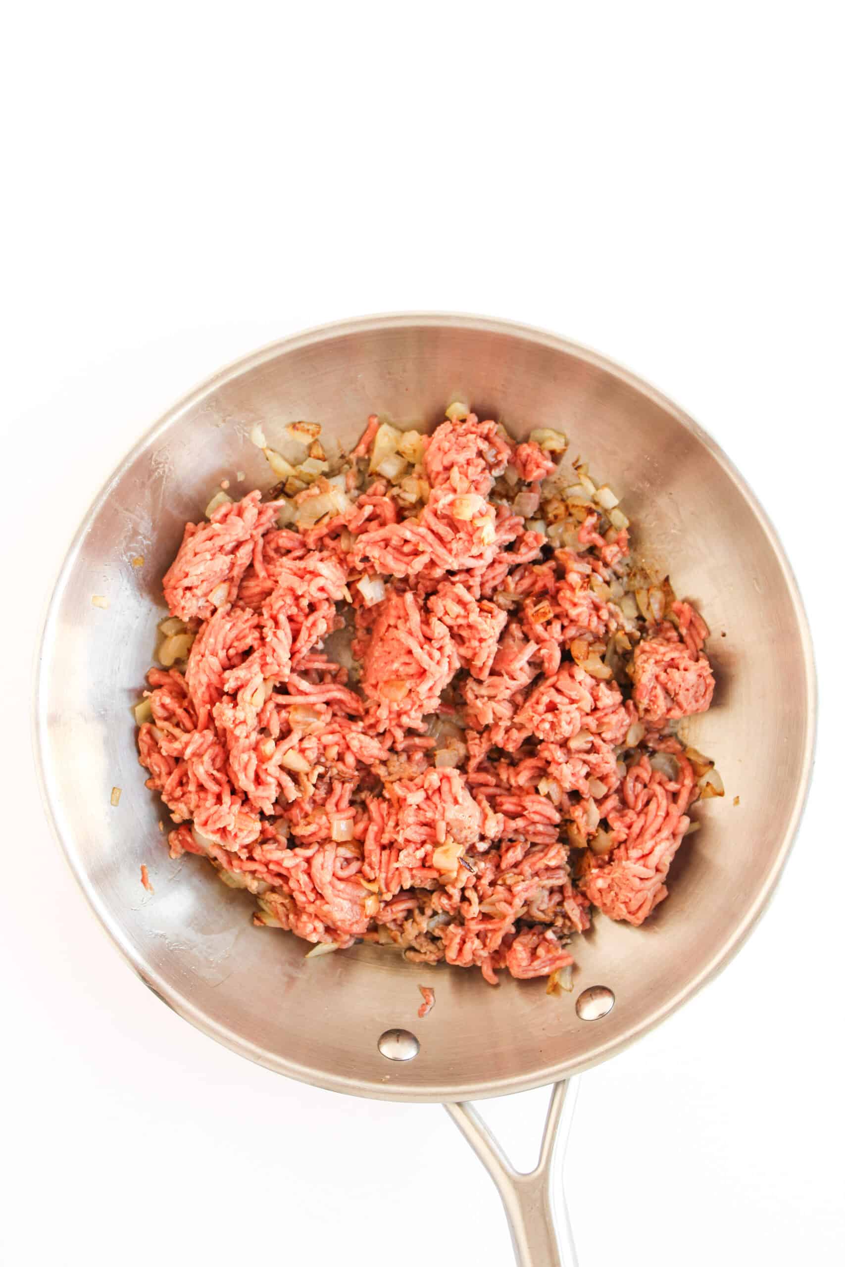 Ground beef cooking with diced onion in a skillet.