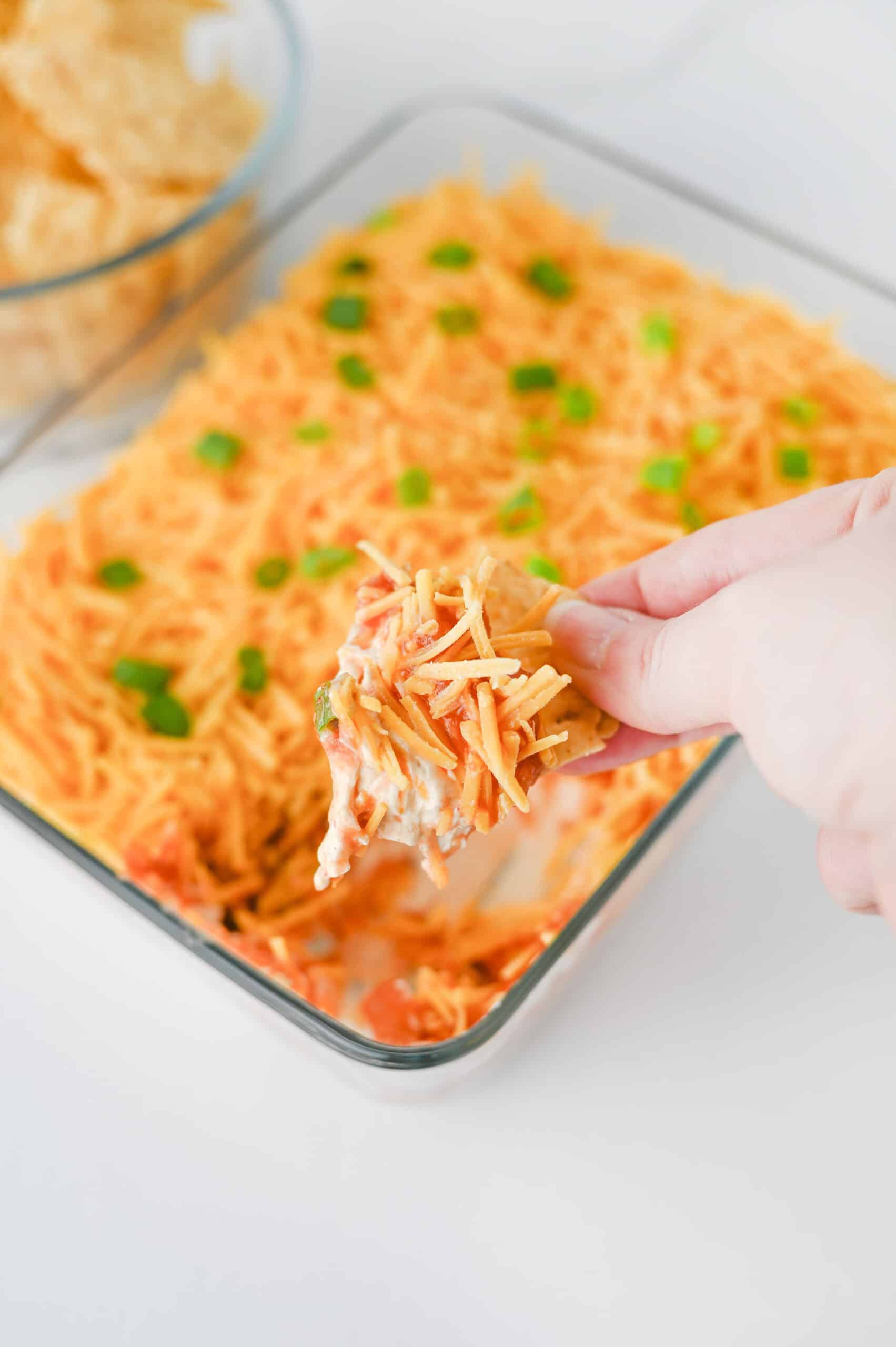 A tortilla chip scooping layered high protein nacho dip.