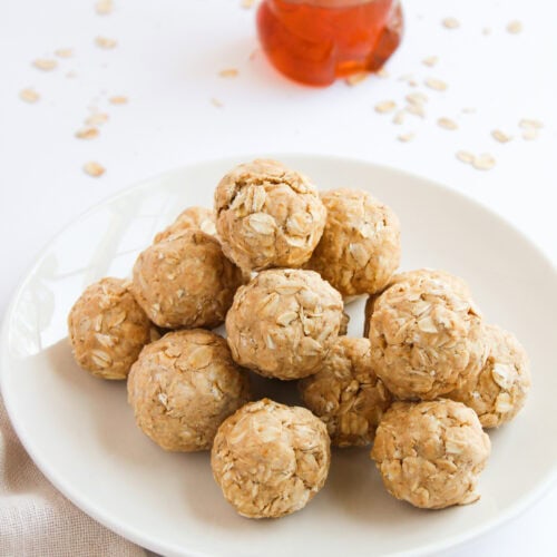 Peanut butter and oats protein bites piled on a white plate with honey and oats.