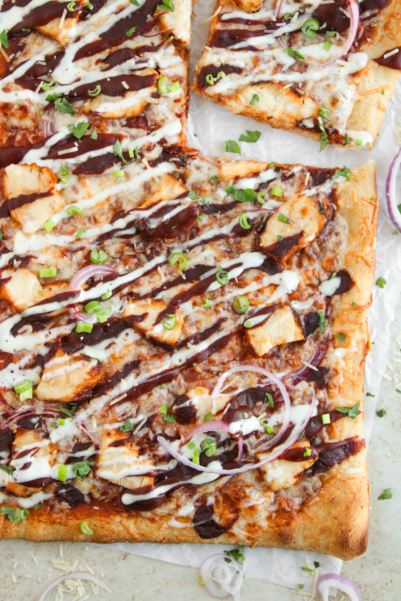 Close-up of sheet pan BBQ chicken pizza with melted cheese, red onion, ranch, and barbecue sauce.