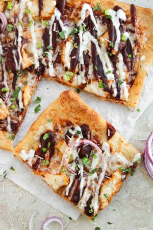 Slices of sheet pan BBQ chicken pizza topped with red onion, ranch, barbecue sauce, and herbs.