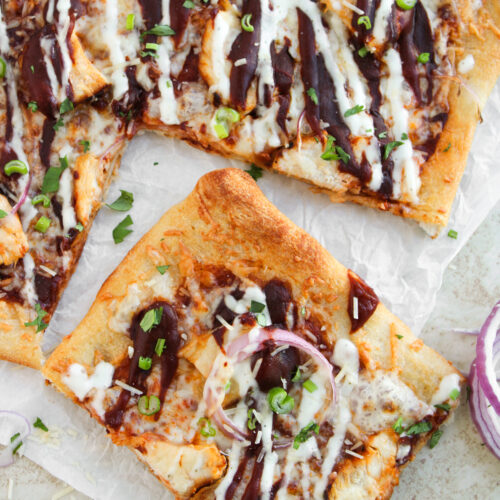Slices of sheet pan BBQ chicken pizza topped with red onion, ranch, barbecue sauce, and herbs.
