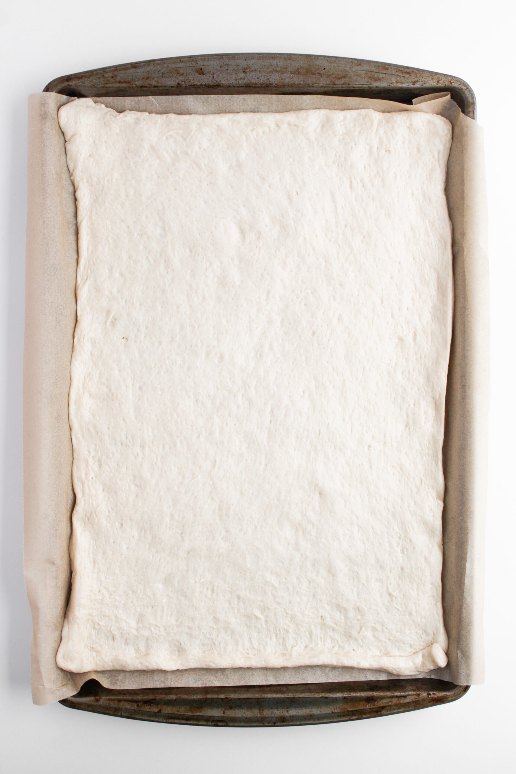 Pizza dough stretched into a parchment-lined sheet pan.