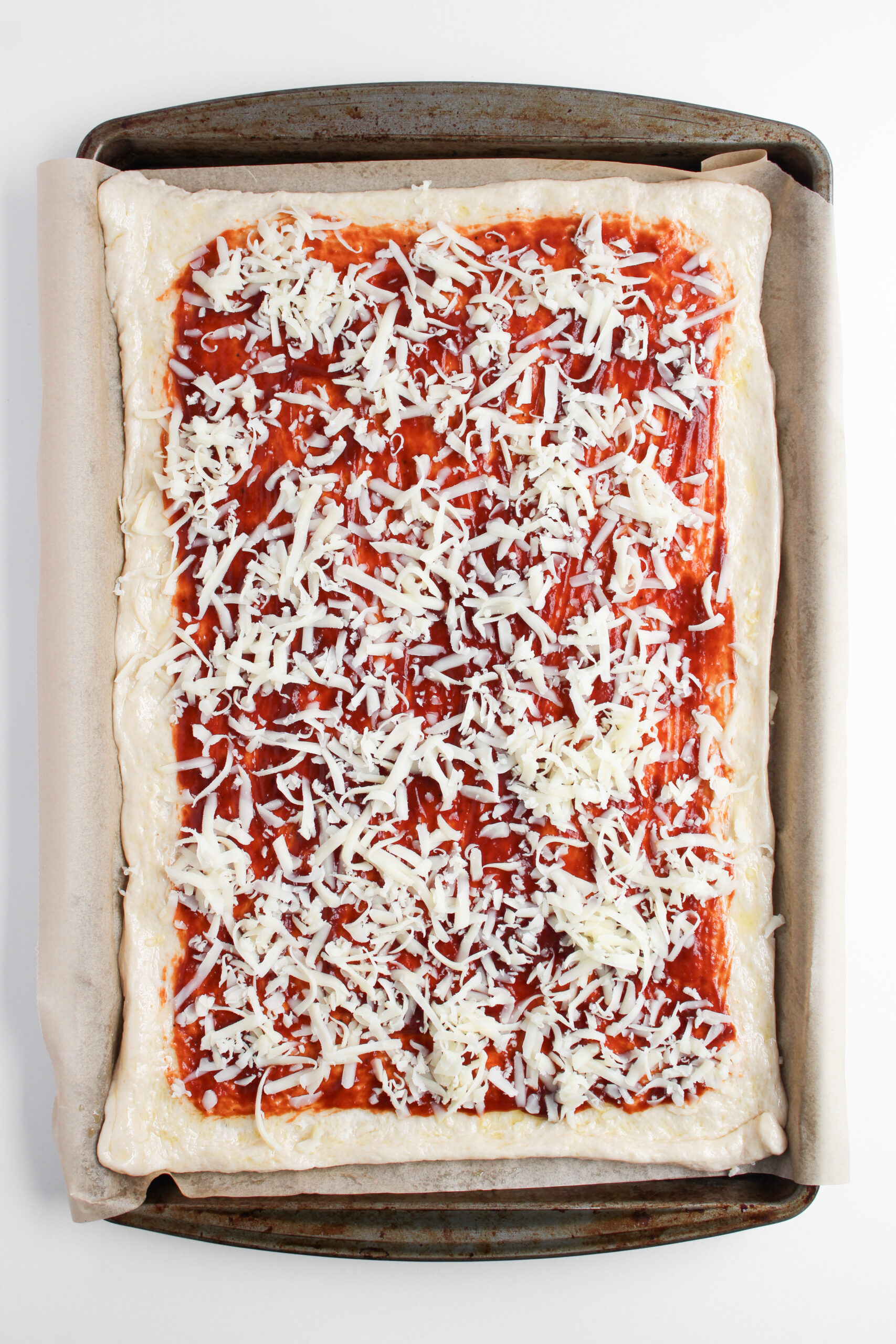 Sheet pan pizza dough topped with barbecue sauce and shredded mozzarella cheese.