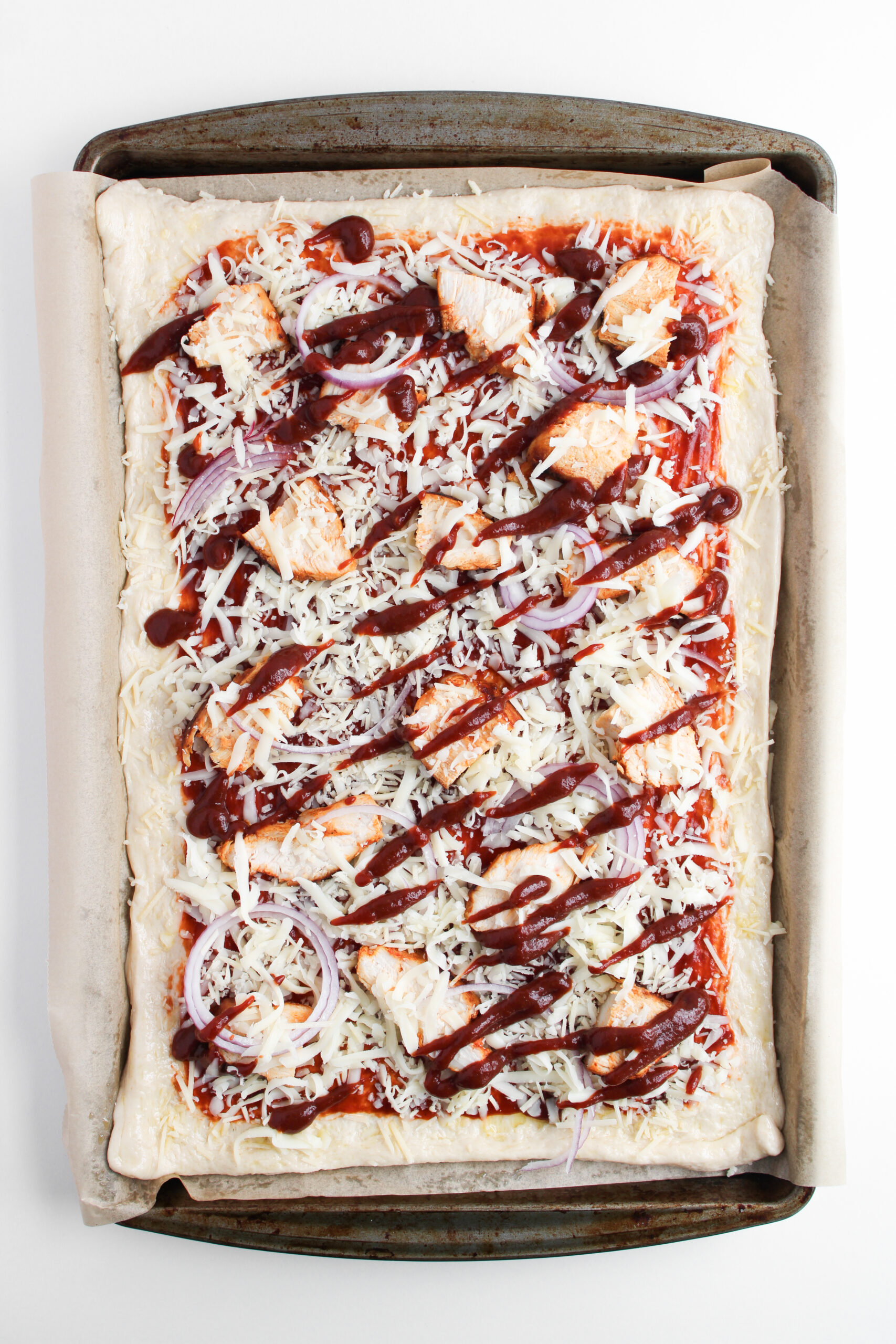 Sheet pan pizza topped with cooked chicken, red onion, cheese, and barbecue sauce.