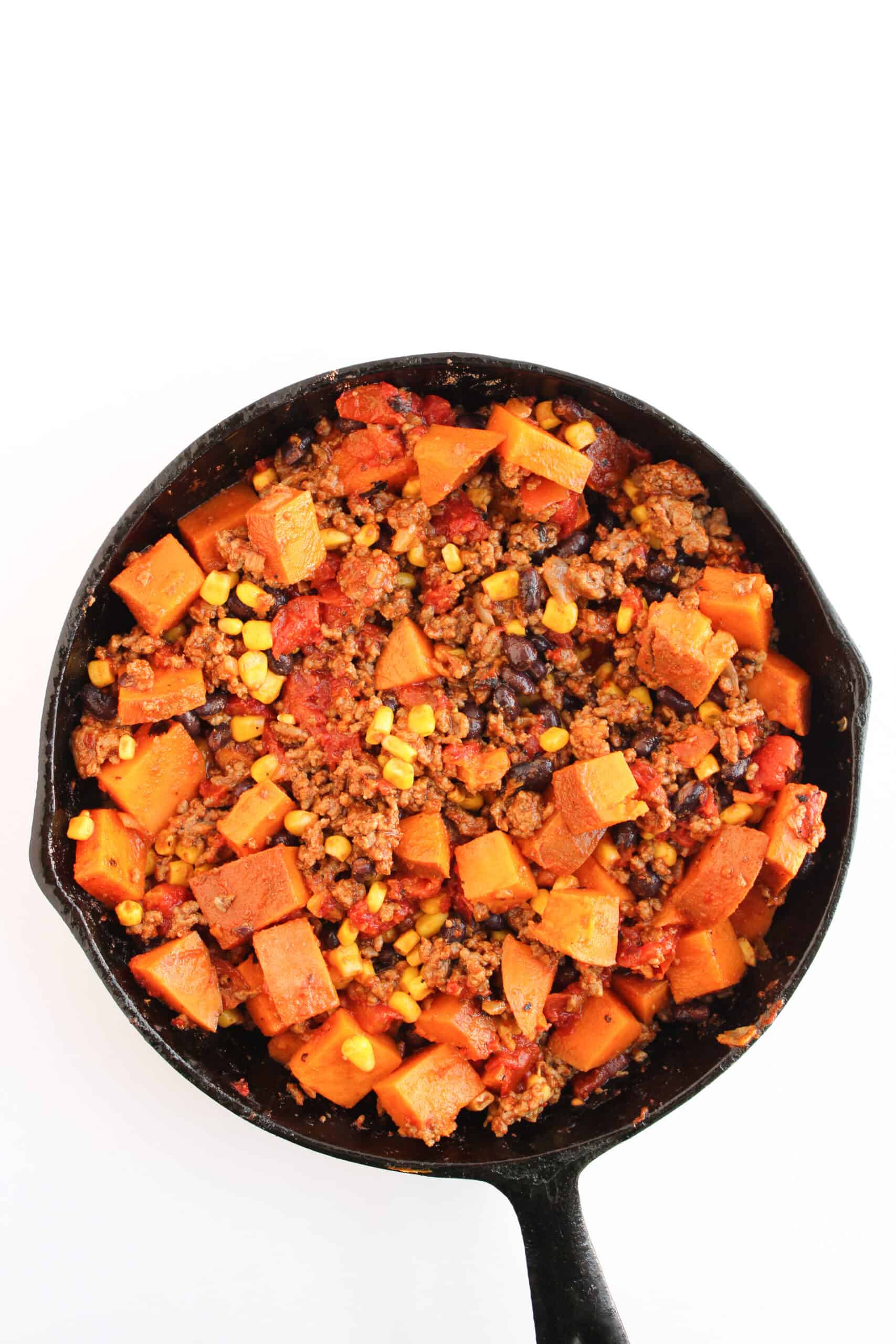 Ground beef, sweet potatoes, corn, black beans, and tomatoes combined in a cast iron skillet.