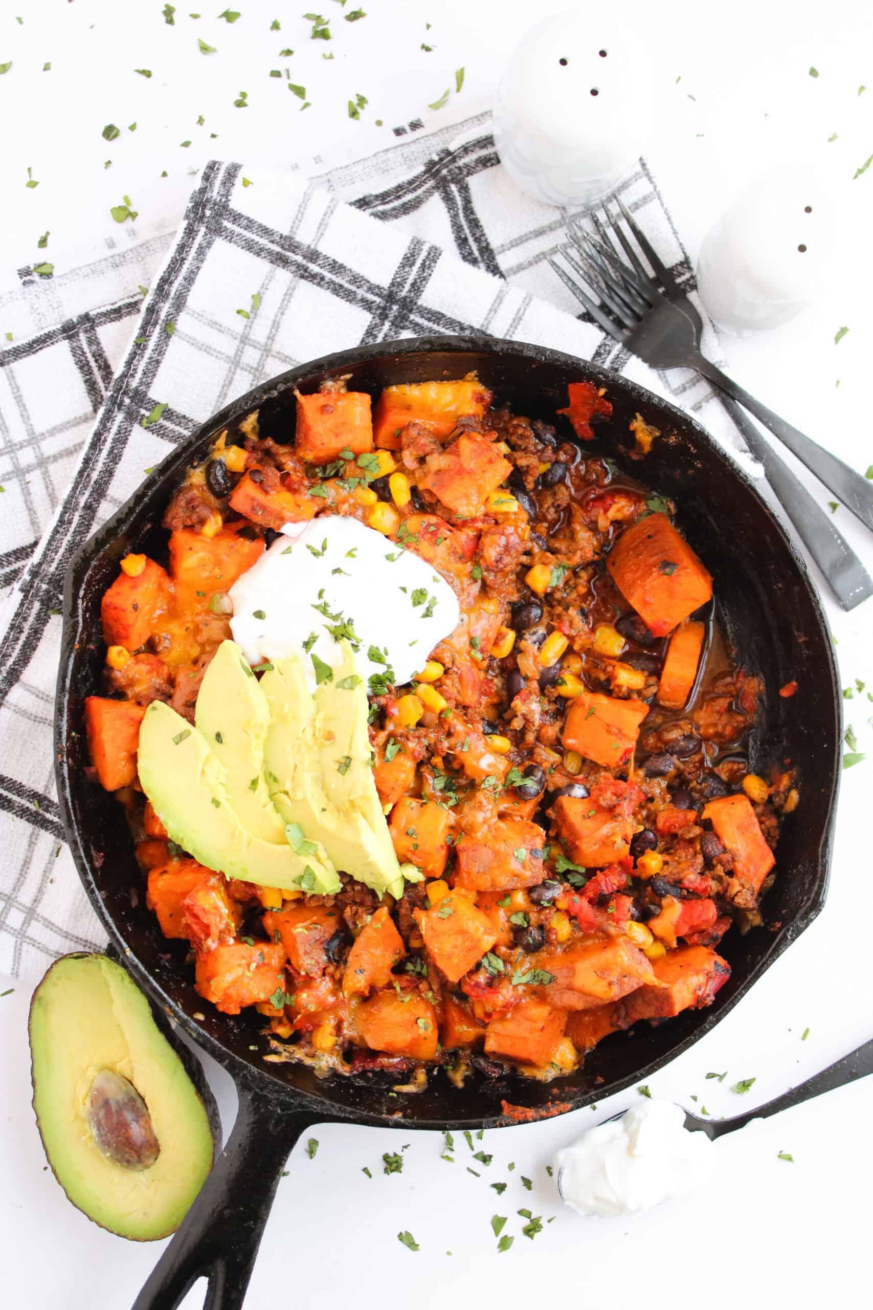 Sweet potato taco skillet topped with avocado, sour cream, and herbs.