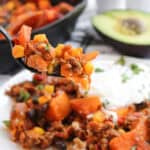 A forkful of sweet potato taco skillet with ground beef, corn, black beans, and melted cheese.